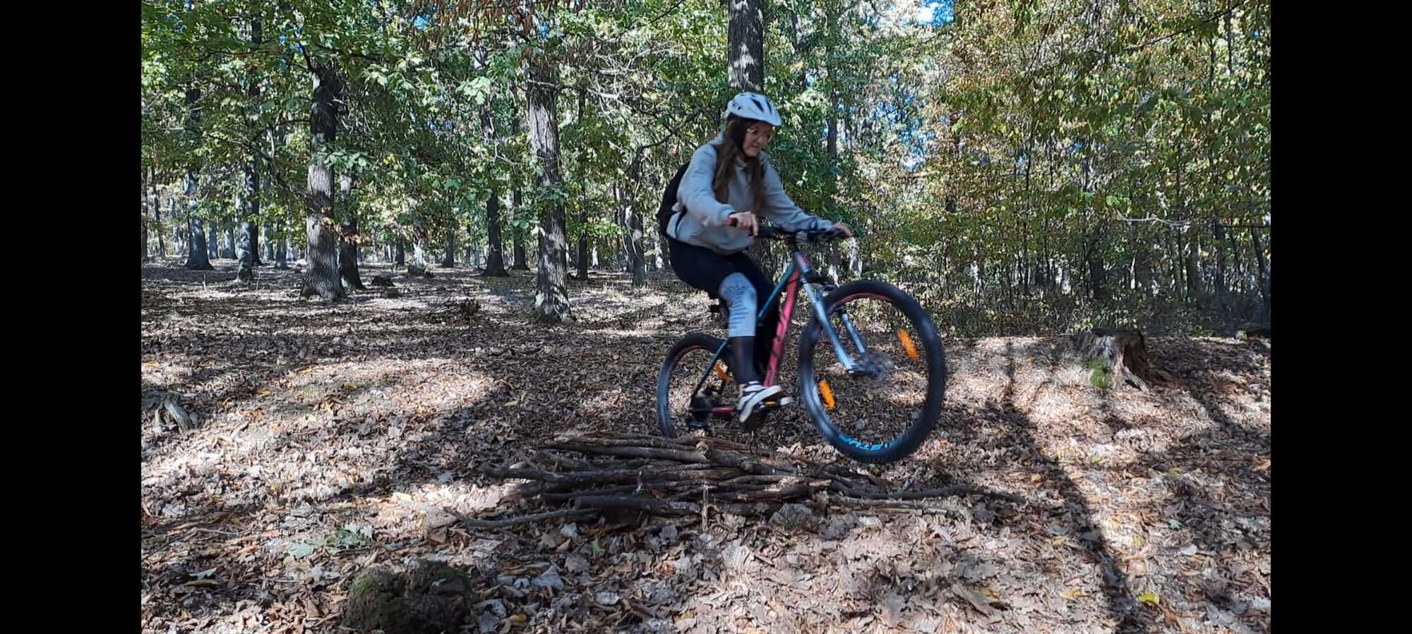 Frau mit Helm fährt Mountainbike über Holzstapel in herbstlichem Wald